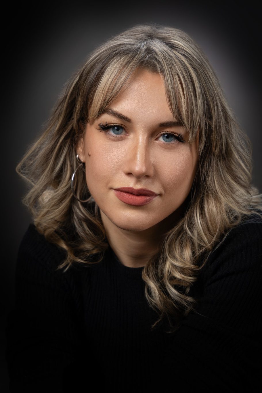 Portrait d'une femme aux cheveux blonds, avec un regard expressif sur fond sombre.