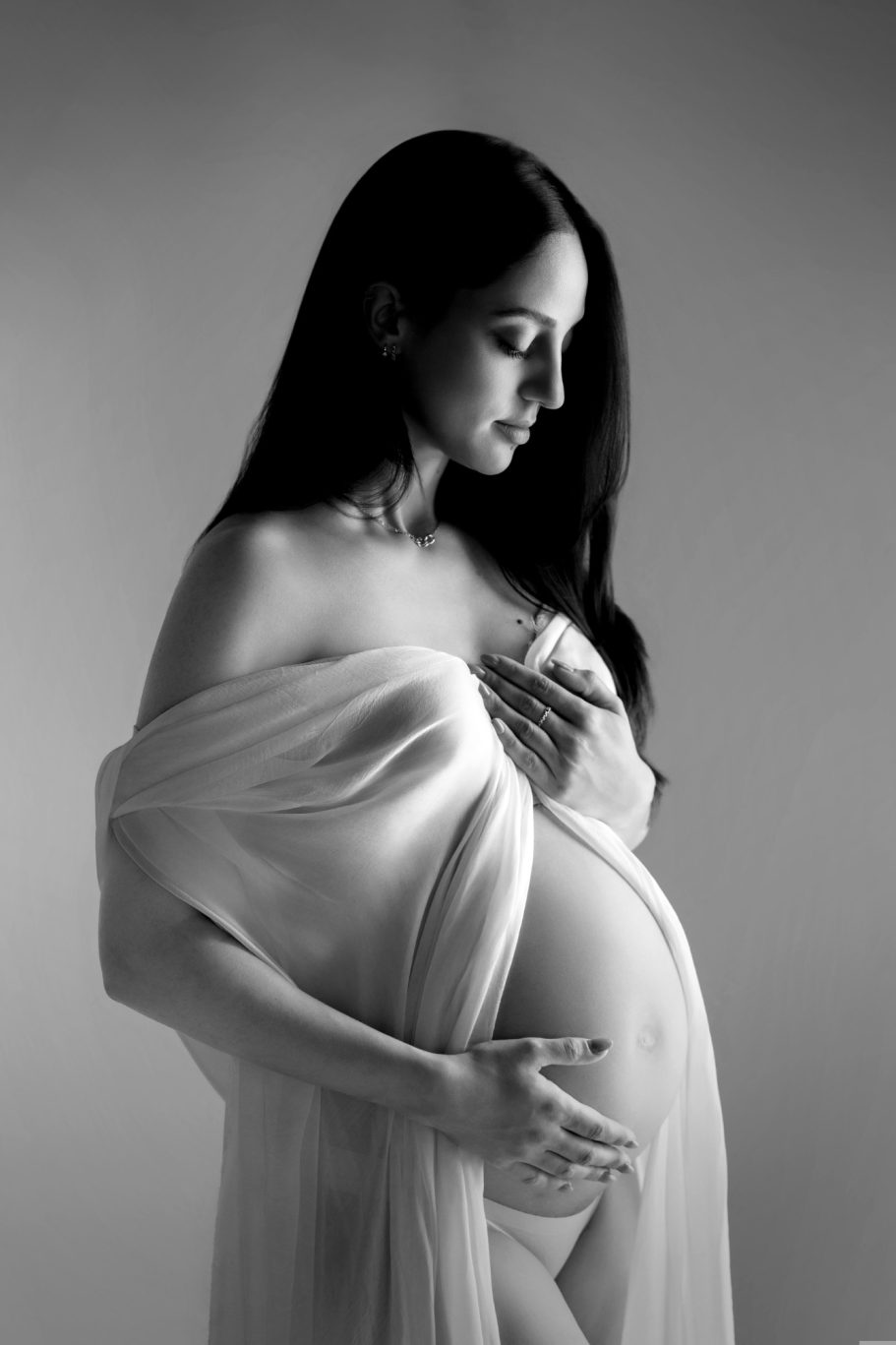 Femme enceinte, vêtue d'un drapé léger, caressant son ventre, en noir et blanc.