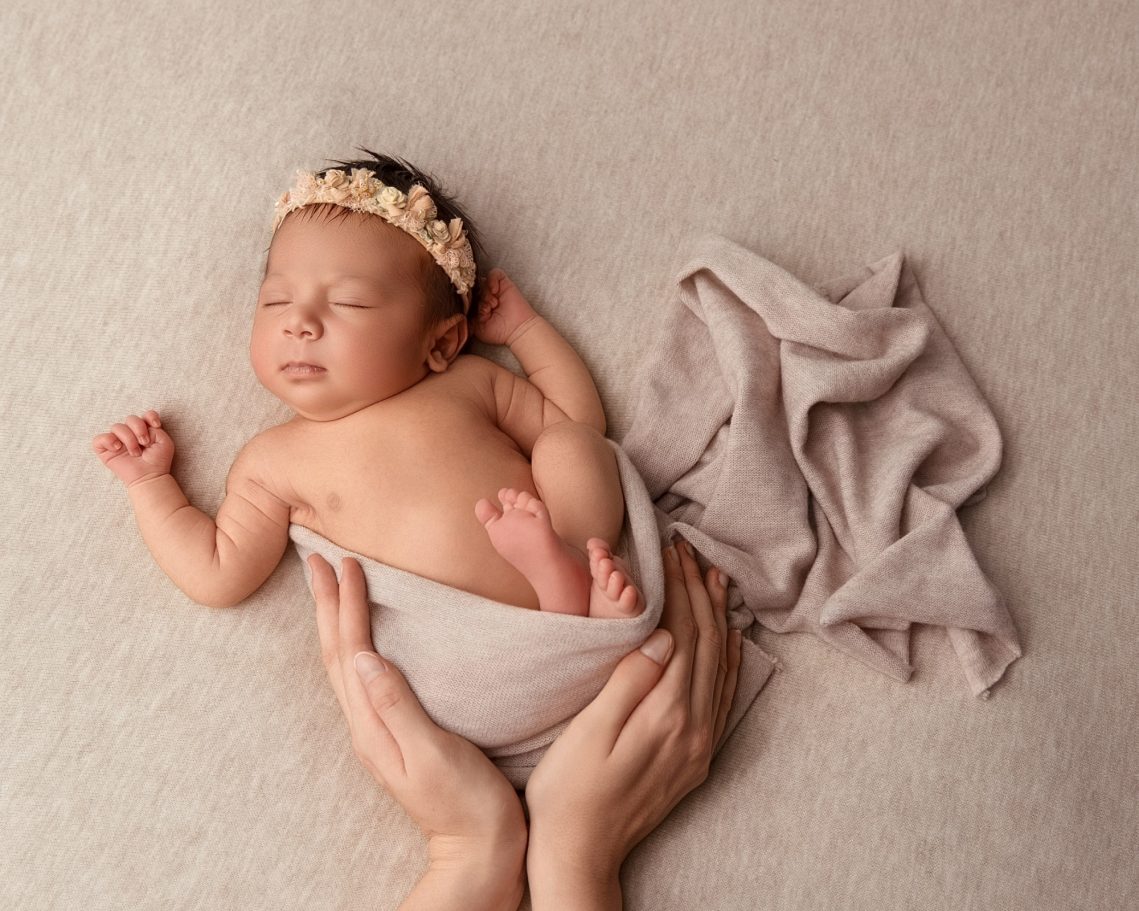 Bébé endormi enroulé dans un tissu, avec un diadème floral sur la tête.